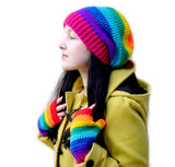 Tamsyn, a white woman with long black hair is wearing a yellow duffle coat, a rainbow striped slouchy crochet beanie and rainbow striped crochet fingerless gloves by VelvetVolcano