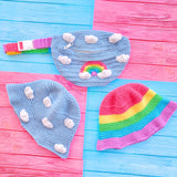 3 kawaii crochet items including a light blue bum bag with pastel rainbow and cloud design, a light blue bucket hat with cloud print and a pastel rainbow striped bucket hat - all pieces by VelvetVolcano