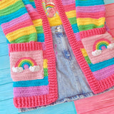A close up of the baby pink square pockets with pastel rainbow and cloud motif on the VelvetVolcano Pastel Rainbow Striped Hooded Cardigan with Rainbow Cloud Pockets