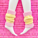 A pair of crochet leg warmers in pastel yellow with baby pink cuffs by VelvetVolcano. The background is pink brick.