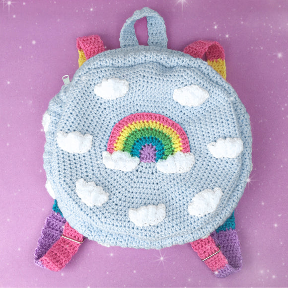 Light blue crochet circular backpack with pastel rainbow striped straps and a pastel rainbow and cloud design on the front by VelvetVolcano