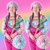Tamsyn (a white woman in her early 30's with long plaited brown hair) is wearing a VelvetVolcano pastel rainbow outfit with cropped crochet sweater, circular shoulder bag and beret and hot pink Lucy & Yak dungarees