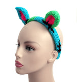 Half neon green and half turquoise cat ear headband with each ear being the opposite colour to the side it is on. The inner ears are neon pink and there are black embroidered stitch marks to look like the cat has been pieced together. FrankenKitty Crochet Headband by VelvetVolcano