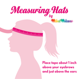 Measuring hats graphic by VelvetVolcano which shows an illustrated head with a tape measure wrapped around it and text that says “place the tape measure about 1 inch above the eyebrows and just above the ears” 
