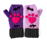 A set of crochet fingerless gloves with a Frankenstein's Monster & Zombie Cat inspired design, with one lilac glove, one violet glove, black embroidered stitch details and cuffs and hot pink heart shaped paws - NecroKitty Fingerless Gloves by VelvetVolcano