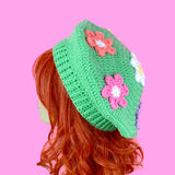 Pastel green crochet beret with 6 daisy appliques, a standard white and yellow daisy in the centre with Peach, Pastel Yellow, Turquoise, Lilac and Bubblegum Pink daisies (all with white centres) in a circle around the centre daisy. Pastel Rainbow Daisy Daze Beret by VelvetVolcano