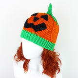 Halloween inspired orange crochet hat with contrasting neon green ribbed bottom section, neon green stem and a black carved jack o' lantern face on the main part of the hat. Pumpkin Beanie by VelvetVolcano