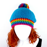Blue slouchy crochet bobble hat with rainbow pom pom and rainbow striped brim by VelvetVolcano